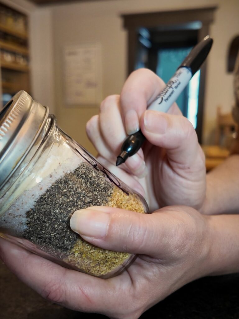Writing a label with a marker on a jar of layered lemon pepper seasoning