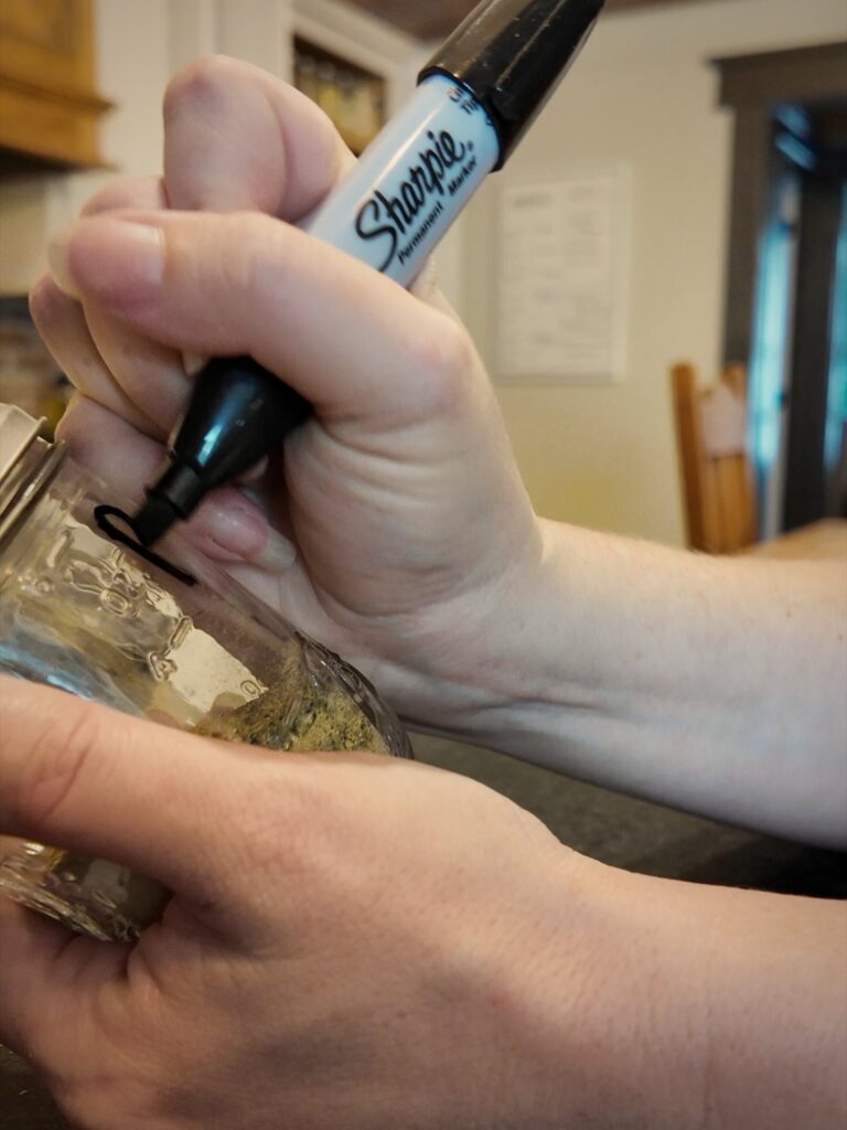 Hand writing a label on a glass jar of poultry seasoning with a black permanent marker