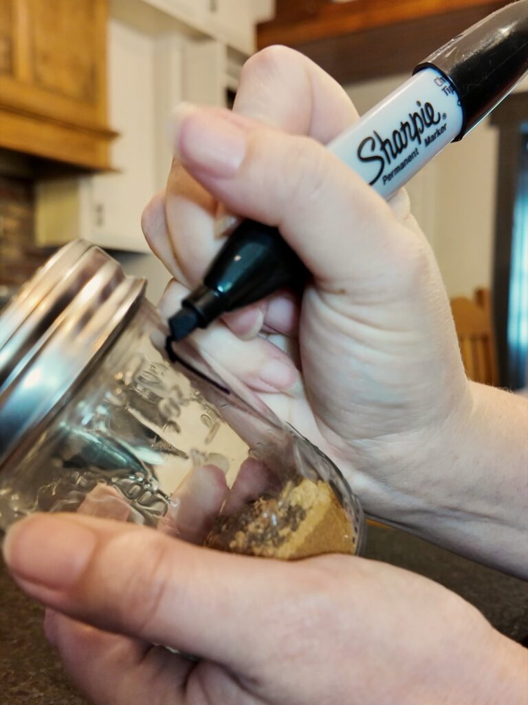 Hand labeling a small glass jar of homemade pumpkin pie spice with a black marker