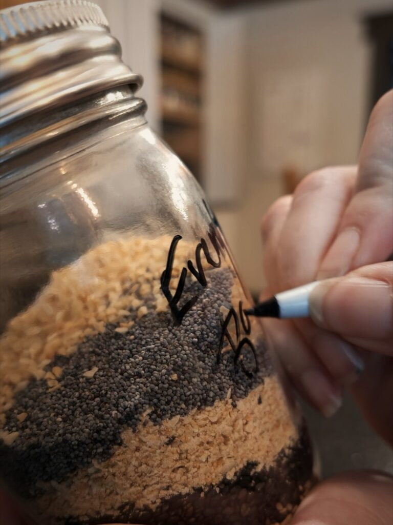 Hand writing a label on a glass jar layered with seeds and dried onion