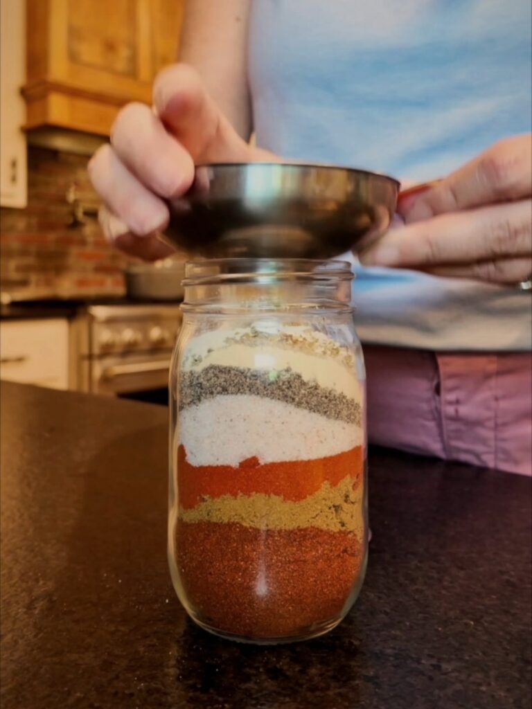 Spices layered in a glass jar as more are added through a funnel