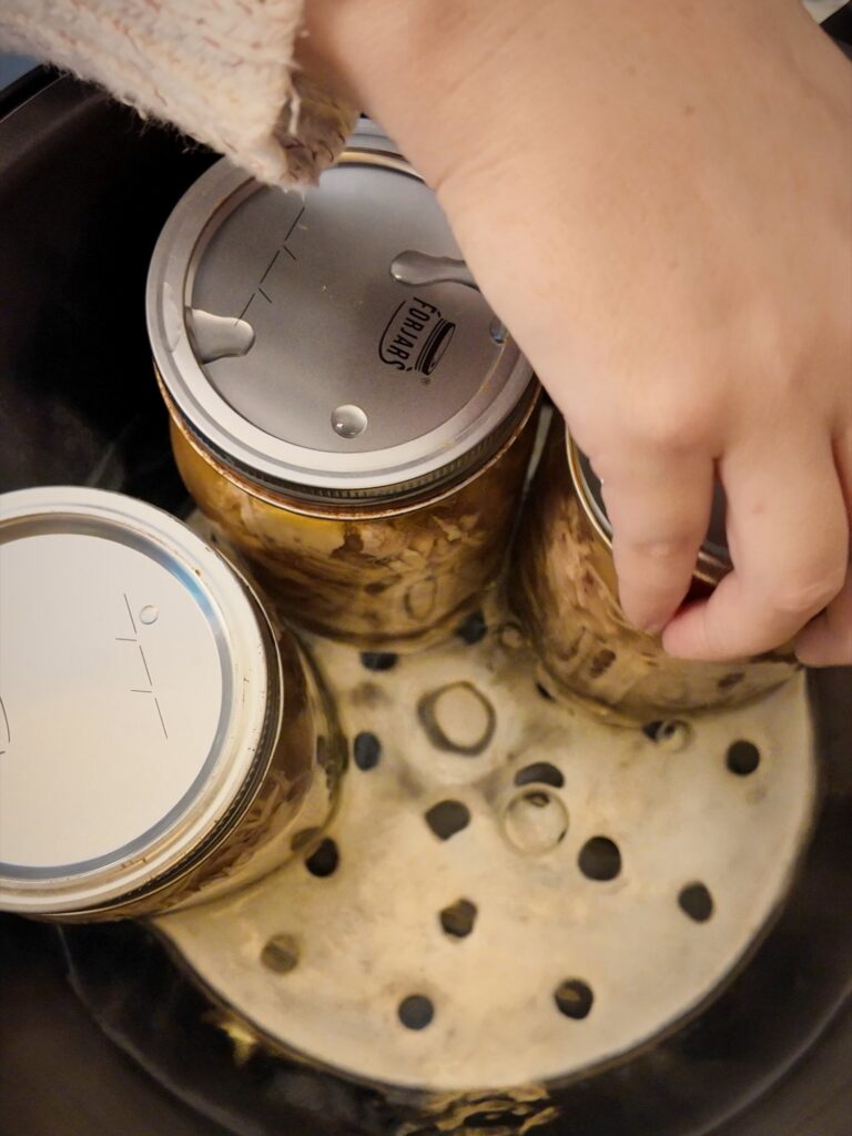 Hand placing lidded jars of chicken onto the rack inside a Presto digital pressure canner