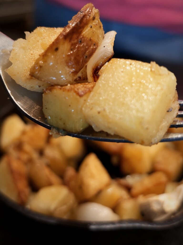 Spoonful of browned potatoes over a cast iron skillet of seasoned potatoes