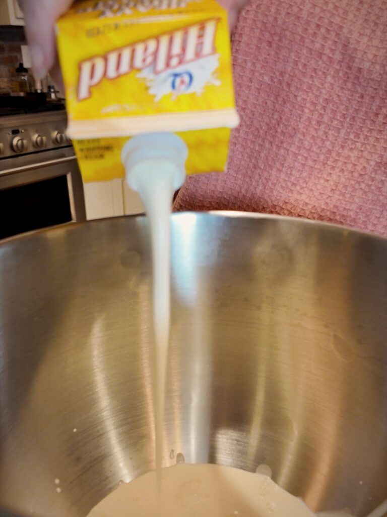 Heavy whipping cream pouring from a carton into a stainless steel mixing bowl