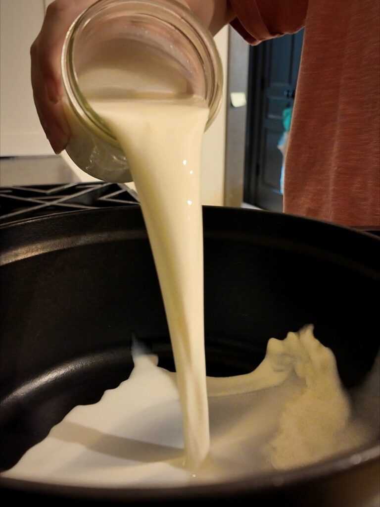 Pouring milk from a glass jar into a dark pan