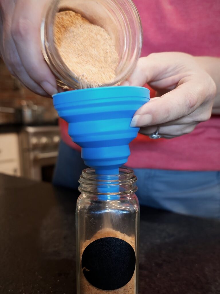 Pouring seasoned salt through a blue funnel into a glass spice jar