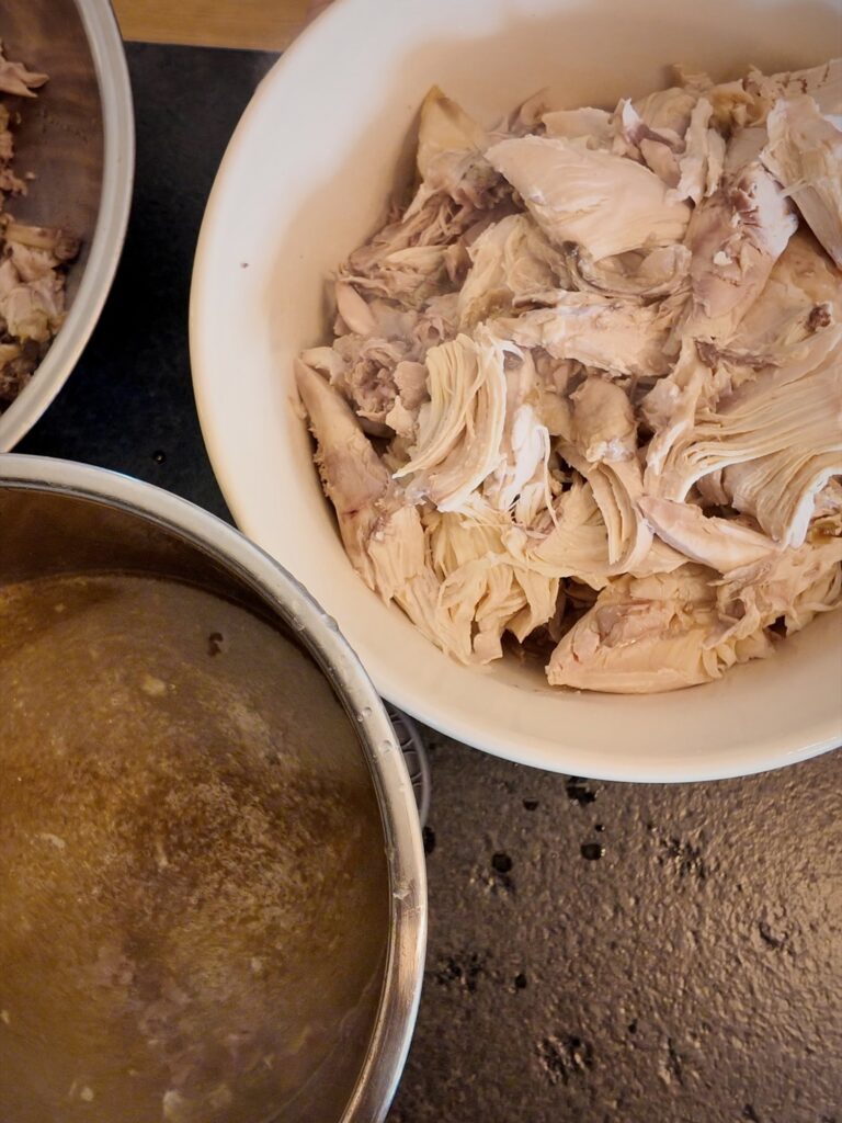 Bowl of chicken pulled into large pieces next to a pot of strained chicken broth