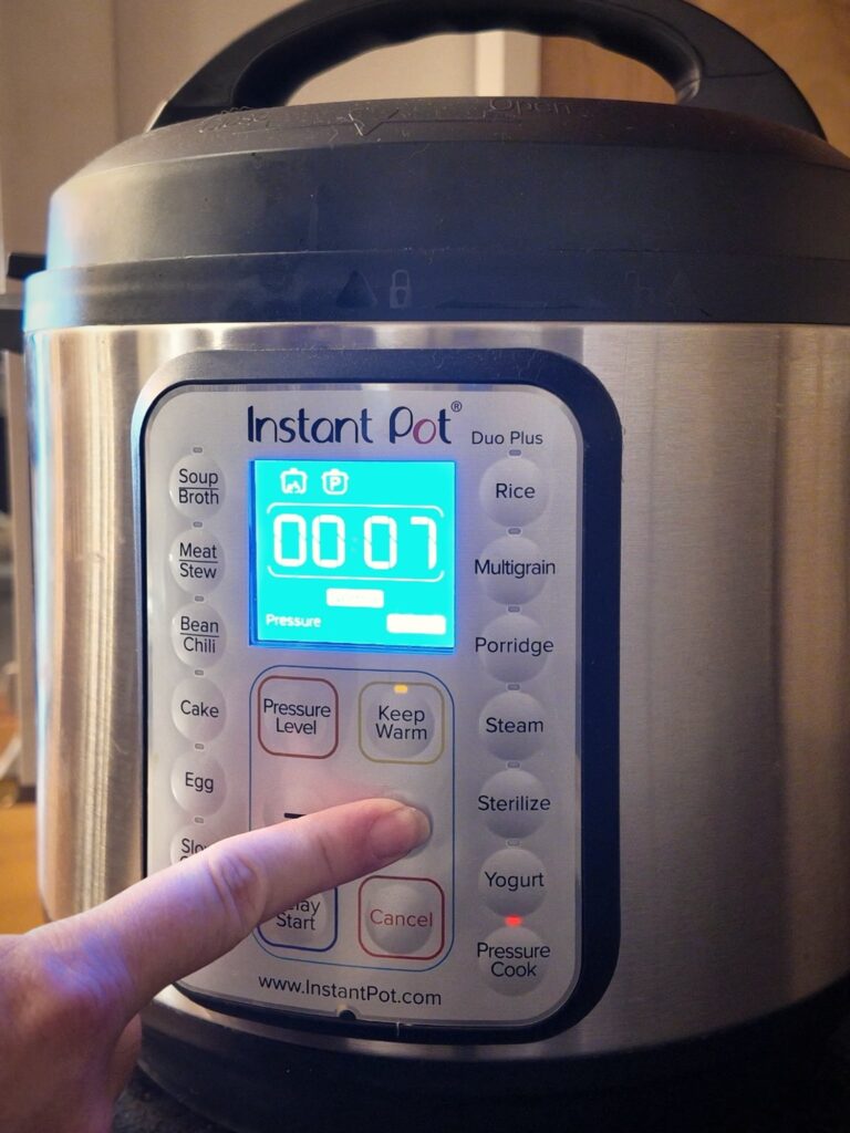 Finger pressing a button on an Instant Pot Duo Plus control panel, with the display showing 00:07.