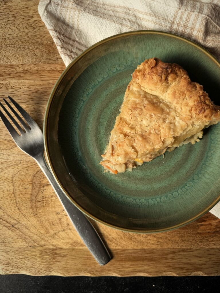 Overhead view of a slice of chicken pot pie on a green plate with a fork on a wooden board