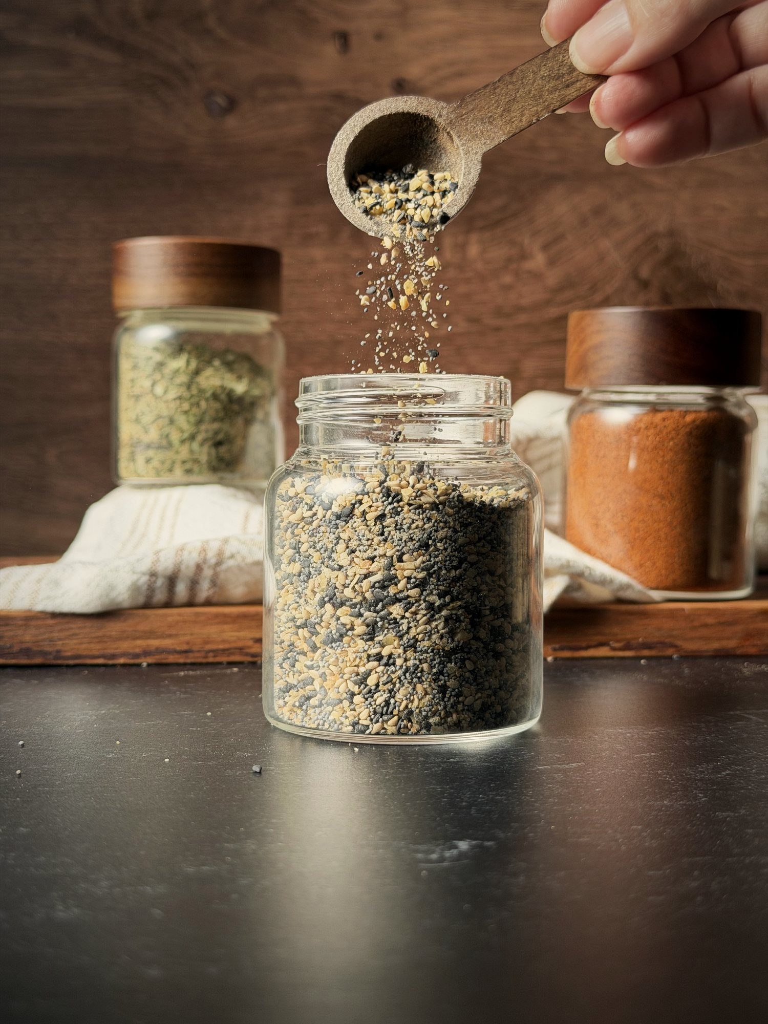 Wooden spoon pouring everything bagel seasoning into a glass spice jar