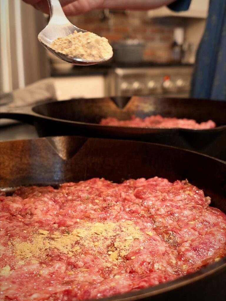 Spoonful of onion soup mix held over ground beef in a cast iron skillet