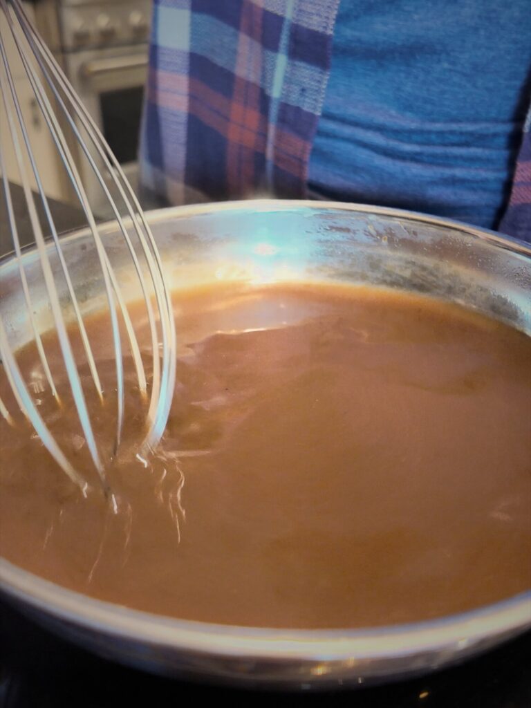 Whisking brown au jus in a stainless steel saucepan